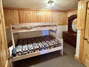 Bedroom featuring wooden walls, a textured ceiling, and carpet flooring