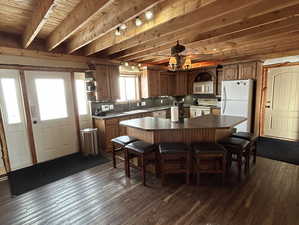 Kitchen with white appliances, a kitchen island, beamed ceiling, and dark wood-style flooring