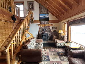 Sitting room with high vaulted ceiling, stairway, wood finished floors, and a wood stove