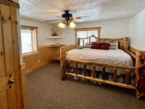 Carpeted bedroom featuring a wainscoted wall, wooden walls, a textured ceiling, and multiple windows