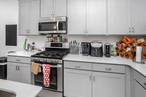 Kitchen featuring light stone countertops, stainless steel appliances, backsplash, and gray cabinetry