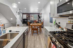 Kitchen with gray cabinetry, stainless steel appliances, light wood finished floors, and decorative backsplash