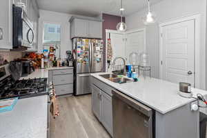 Kitchen with light wood finished floors, appliances with stainless steel finishes, a kitchen island with sink, gray cabinetry, and a sink