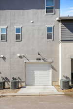 Exterior space featuring a garage, cooling unit, and stucco siding