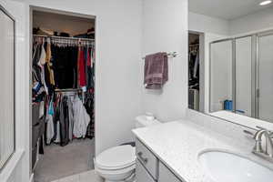 Bathroom with a stall shower, vanity, toilet, and a walk in closet