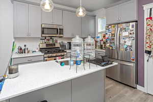 Kitchen featuring appliances with stainless steel finishes, light wood-type flooring, gray cabinets, and light stone counters