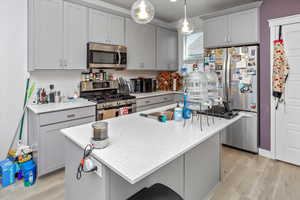 Kitchen with light stone counters, a kitchen island with sink, gray cabinetry, appliances with stainless steel finishes, and light wood-type flooring