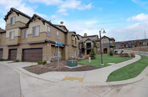 View of property with a garage, concrete driveway, stone siding, a residential view, and a front lawn