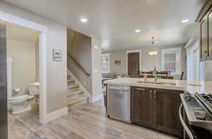 Kitchen featuring stainless steel appliances, light countertops, a sink, dark brown cabinetry, and light wood-type flooring