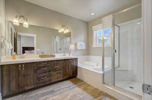 Ensuite bathroom featuring double vanity, a stall shower, wood finished floors, a garden tub, and a sink