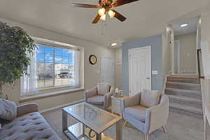 Carpeted living room featuring ceiling fan, stairway