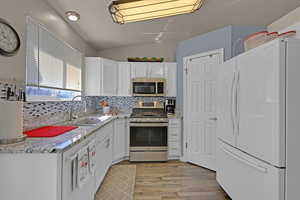 Kitchen with decorative backsplash, stainless steel appliances, light wood-type flooring, white cabinetry, and a sink