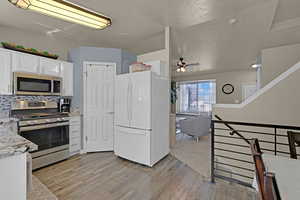 Updated Kitchen featuring stainless steel appliances, white cabinetry, light wood-style floors, and light stone countertops