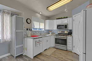 Kitchen featuring a sink, white cabinets, appliances with stainless steel finishes, light wood finished floors, and tasteful backsplash