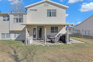 Rear view of property with a patio area, fence, and a lawn