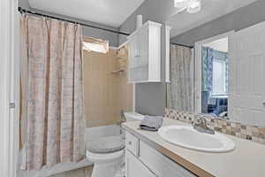 Bathroom with toilet, shower / bathtub combination with curtain, backsplash, and vanity