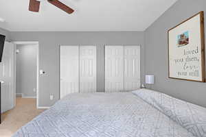 Carpeted bedroom with a ceiling fan, two closets