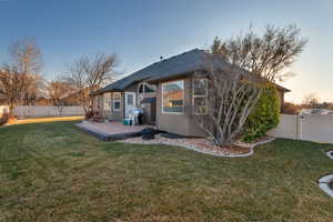 Back of property at dusk with a fenced backyard, a lawn, and stucco siding