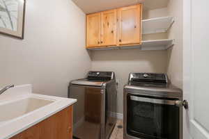 Laundry area with cabinet space, baseboards, tile patterned floors, independent washer and dryer, and a sink