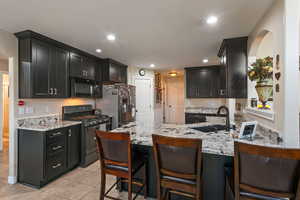 Kitchen featuring black microwave, dark cabinets, a sink, stainless steel refrigerator with ice dispenser, and gas range