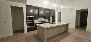 Kitchen with a center island with sink, light wood finished floors, stainless steel appliances, backsplash, and glass insert cabinets