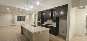 Kitchen featuring a center island with sink, visible vents, stainless steel appliances, light wood-style floors, and a sink