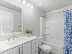 Full bathroom featuring shower / tub combo with curtain, a textured ceiling, toilet, and vanity