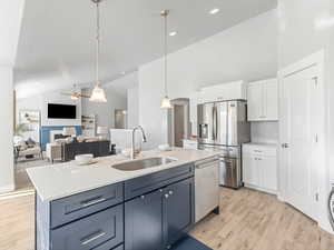 Kitchen with stainless steel appliances, a sink, white cabinets, light countertops, and light wood finished floors