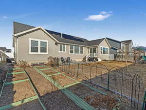 Back of property featuring a playground, a vegetable garden, stucco siding, roof mounted solar panels, and fence