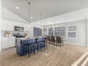Kitchen featuring a chandelier, light wood-style flooring, a kitchen breakfast bar, white cabinets, and appliances with stainless steel finishes