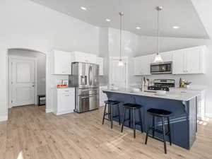 Kitchen with arched walkways, stainless steel appliances, a breakfast bar, white cabinets, and light wood-style floors
