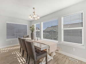 Dining room with light wood-style floors, visible vents, a notable chandelier, and baseboards