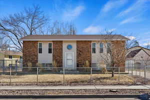 Bi-level home featuring a fenced front yard, brick siding, and a shingled roof