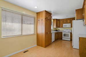 Kitchen with light wood-type flooring, white appliances, visible vents, and brown cabinetry