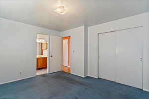 Unfurnished bedroom featuring carpet, a closet, a textured ceiling, and ensuite bathroom