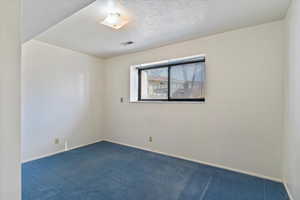 Spare room with baseboards, visible vents, dark carpet, and a textured ceiling