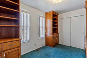 Unfurnished bedroom featuring a closet, visible vents, dark carpet, and a textured ceiling