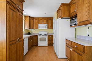 Kitchen with white appliances, brown cabinetry, and a sink