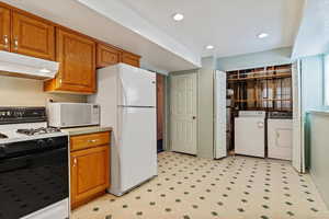 Kitchen with brown cabinets, light floors, washer and dryer, white appliances, and under cabinet range hood