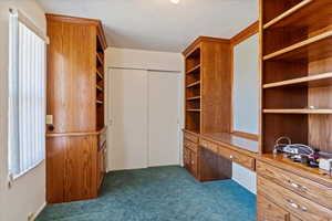 Walk in closet featuring dark colored carpet and built in desk