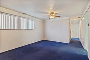 Empty room with baseboards, dark carpet, visible vents, and a ceiling fan