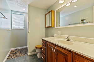 Bathroom with toilet, vanity, a textured ceiling, baseboards, and tile patterned floors