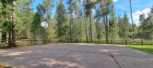 View of patio with basketball hoop, fence, and a wooded view