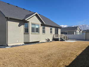 Back of house featuring fence, a mountain view, a lawn, and stucco siding