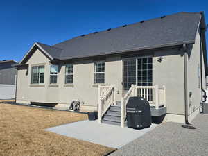 Rear view of property with a patio area, a shingled roof, stucco siding, and a yard