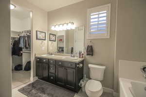 Bathroom featuring a bath, double vanity, toilet, and a sink