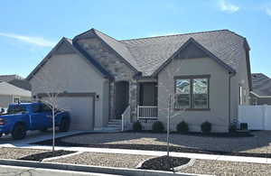 View of front of home featuring a garage, stone siding, roof with shingles, and fence