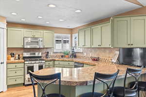 Kitchen featuring appliances with stainless steel finishes, a kitchen breakfast bar, a peninsula, and green cabinets