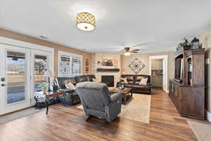 Living area featuring baseboards, ceiling fan, a textured ceiling, light wood-style floors, and a fireplace