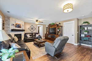 Living area featuring baseboards, visible vents, ceiling fan, wood finished floors, and a fireplace